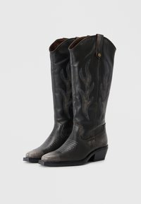 Black leather cowboy boots with flame embroidery, pointed toe, and a low stacked heel. Includes brown accents and a button detail at the top.