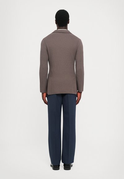 Brown knit blazer with a tailored shape, single vent at the back, paired with navy wide-leg trousers and black shoes.