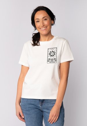 T-shirt en coton blanc avec un design imprimé de carte de tarot comprenant un motif de soleil et des fleurs, manches courtes et encolure ras du cou.