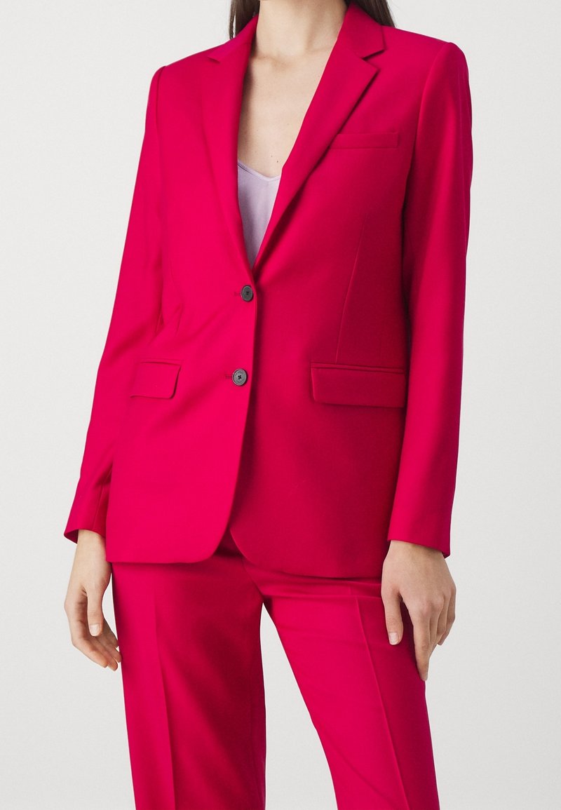 Kirkkaan vaaleanpunainen blazer, jossa on muotoiltu istuvuus, yksirivinen malli, kaksi etutaskua ja lovikaulus. Sujuva, kevyt kangas.
