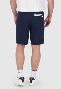 Pantaloni corti navy in tessuto leggero con una cintura elastica, dotati di una tasca posteriore con dettaglio di zip bianca. Abbinati a scarpe bianche.
