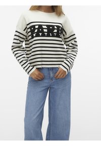 Pull tricoté à rayures blanches et noires avec le logo "PAPER" au centre. Ajusté aux poignets, associé à un jean large bleu clair.