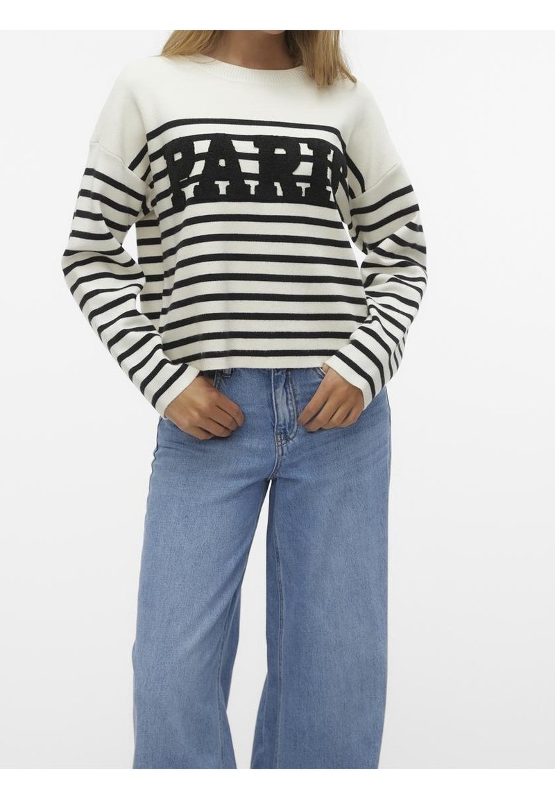 Pull tricoté à rayures blanches et noires avec le logo "PAPER" au centre. Ajusté aux poignets, associé à un jean large bleu clair.