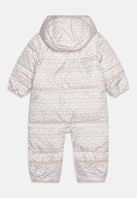 Combinaison de neige rembourrée beige clair avec un motif géométrique blanc, une capuche, des poignets élastiques et une fermeture éclair intégrale pour un enfilage facile.