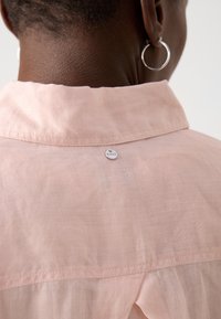 Camicia rosa chiaro con una consistenza morbida, dotata di colletto e di una piccola etichetta argentata con la scritta "BOSS" vicino al collo.
