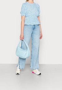 Haut à imprimé floral bleu clair avec manches bouffantes, associé à un jean en denim clair taille haute. Accessoirisé d'un sac à main bleu clair et de baskets.