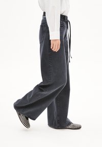 Grijze denim jeans met een hoge taille en een trekkoord, met een lichte vervaging. Gecombineerd met zwarte flats versierd met zilveren studs.