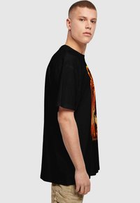 Black cotton t-shirt featuring a vibrant graphic on the front, short sleeves, and a relaxed fit. Displayed on a model from the side.