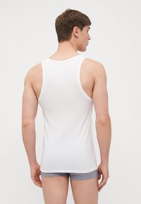 Weißes Tanktop aus weicher Baumwolle, mit klassischem ärmellosem Design, rundem Ausschnitt und tailliertem Schnitt, von hinten betrachtet.