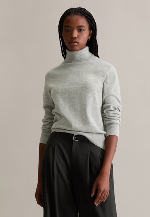 Hellgrauer, gestrickter Rollkragenpullover mit gerippten Bündchen und Saum, kombiniert mit hochgeschnittenen schwarzen Hosen, die einen schwarzen Gürtel und Falten aufweisen.