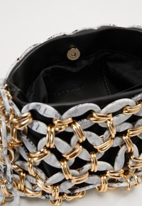 Czarna torba z zapięciem na magnes, ozdobiona dekoracyjnym łańcuchem z białych, marmurowych ogniw i złotych łączników wokół zewnętrznej części.