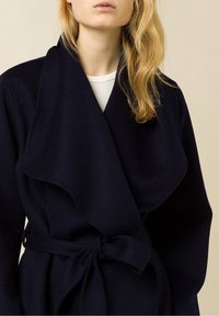 Abrigo envolvente de lana en color marino con un gran cuello con muescas, mangas anchas y un cinturón atado en la cintura, con una textura suave y un diseño minimalista.
