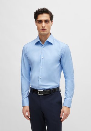 Camicia a maniche lunghe azzurra chiaro con colletto, design fitted, bottoni frontali, texture liscia, abbinata a pantaloni scuri e una cintura nera.
