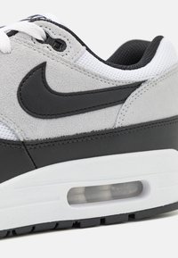 Gray suede and black leather sneaker with white mesh accents. Features a visible air unit and a black swoosh logo on the side.