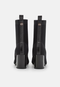 Schwarze Ankle Boots mit einem gerippten Strickoberteil und glatten Lederakzenten. Chunky schwarze Absätze und eine Lasche hinten für einfaches Anziehen.