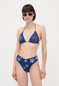 Blauwe denim bikini met een driehoekige top met meerkleurige borduursels en een high-waisted broekje versierd met grote lichtblauwe sterren.