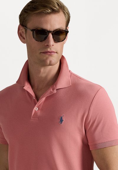 Tricou polo roz din țesătură texturată, cu guler și deschidere cu două butoane; are un accent cu logo albastru pe piept.