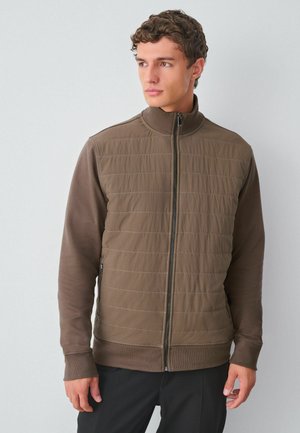 Braune Zip-Jacke mit gepolsterter Front und langen Ärmeln. Verfügt über gerippte Abschlüsse und einen Stehkragen. Glatte Textur mit feinen Nahtdetails.