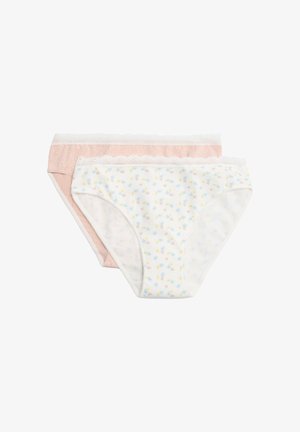 Mujer con sostén blanco y ropa interior blanca con encaje floral, de pie con los brazos relajados contra un fondo liso.