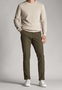 Beige tröja med rund halsringning, tillsammans med olivgröna slim-fit byxor och vita sneakers. Slät textur, enkel design.