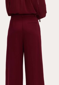 Bordeaux brede bukser med en glat overflade, der har en baglomme og bæltestropper for et skræddersyet udseende.