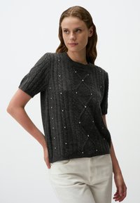 Sweter z krótkim rękawem w ciemnoszarym kolorze, wykonany z dzianiny, z teksturowanym wzorem i rozrzuconymi małymi koralikami. Klasyczny okrągły dekolt z prążkowanymi krawędziami.