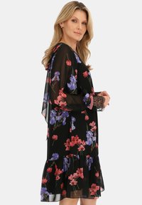 Czarna, kwiecista sukienka z przezroczystego materiału. Posiada purpurowe i czerwone kwiaty, długie rękawy oraz koronkowe akcenty na mankietach. Rozkloszowany, falbaniasty dół.