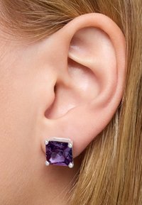 Orecchino a bottone quadrato in ametista incastonato in argento con quattro griffe, caratterizzato da una superficie lucida e una texture liscia, vicino a un orecchio umano.