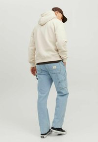 Ljusbeige hoodie som bärs över en mörk tröja, ihop med ljusblå cargobyxor med fickor. Svarta sneakers fulländar outfiten.