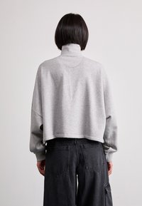 Sudadera gris recortada con cuello alto y mangas largas, combinada con pantalones cargo negros de pierna ancha que cuentan con bolsillos traseros.