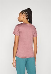 Μακρυμάνικο μπλουζάκι μαρόου το οποίο έχει στρογγυλή λαιμόκοψη, λείο ύφασμα και άνετη εφαρμογή, συνδυασμένο με τιρκουάζ παντελόνια, φαίνεται από πίσω.