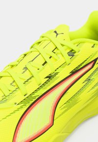 Lys gul sportssko med tekstureret overflade, udstyret med sorte accenter og striber, forstærket tå og neonfarvede snørebånd for en sikker pasform.