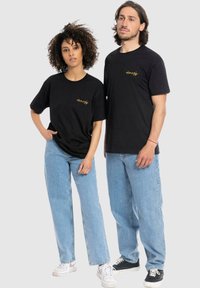Zwarte katoenen T-shirts met korte mouwen, voorzien van een kleine gele grafische afbeelding. Draag het met lichtblauwe rechttoe-rechtaan jeans en casual schoenen.