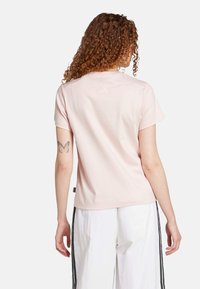 Svetloružová krátkorpásková tričko vyrobené z mäkkej látky, s jemným logom na zadnej strane a voľným strihom. Značka viditeľná na leme.