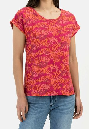 Femme portant une chemise à manches courtes avec un motif rose et orange et une petite poche sur la poitrine, associée à un jean bleu.