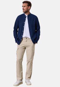 Námořnická košile s knoflíky, bílý tričko, béžové cargo kalhoty s bočními kapsami. Ležérní obuv v bílé barvě s šedými akcenty.