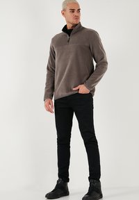 Grå fleece-trøje med halv-lynlås krave, blød tekstur og kontrasterende sorte detaljer, parret med sorte slim-fit bukser og sorte ankelstøvler.