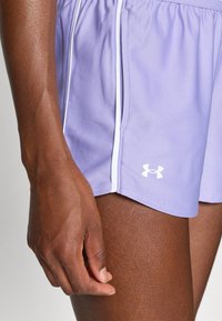 Kadar u kojem se nalazi ruka i but osobe koja nosi svijetlosive sportske kratke hlače s bijelim Under Armour logotipom.