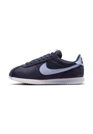 Baskets basses bleu foncé avec un logo Nike bleu clair, semelle blanche et lacets, vues de côté sur fond blanc.