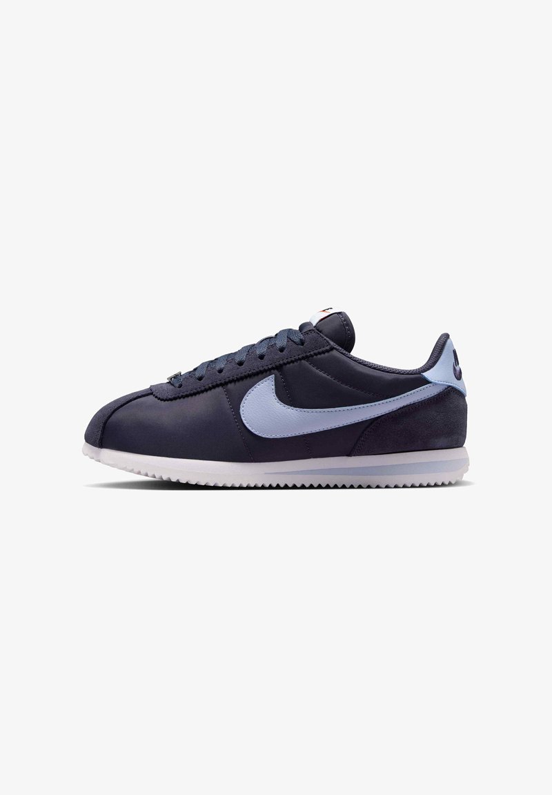 Σκούρο μπλε sneaker χαμηλού ύψους με ανοιχτό μπλε λογότυπο Nike, λευκή σόλα και κορδόνια, εμφανίζεται από το πλάι σε λευκό φόντο.