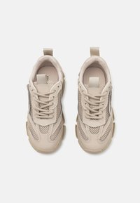 Zapatillas beige confeccionadas con materiales de malla y cuero, punta redonda, suela gruesa y detalles de tela. Cierre con cordones y cinta en la parte trasera.