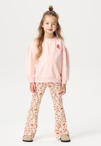 Jasnoróżowy sweatshirt z bufiastymi rękawami i motywem owocowym, w połączeniu z różowymi spodniami w dzwony z kwiatowym i owocowym wzorem.