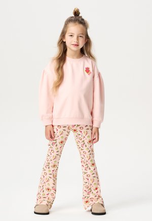 Helles rosa Sweatshirt mit Puffärmeln und einem Obstmotiv, kombiniert mit weit geschnittenen rosa Hosen, die ein Blumen- und Obstmuster aufweisen.