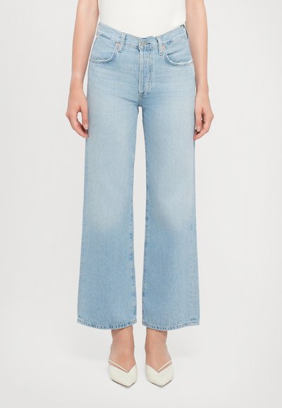 Jeans larghi azzurri realizzati in denim, con vita alta, tasche frontali e orlo pulito. Indossati con scarpe bianche a punta.