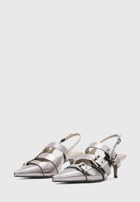 Metallic silver slingback shoes with pointed toes, featuring layered straps and silver hardware accents. Low, slender heels. Smooth texture.
