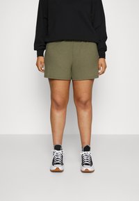 Shorts côtelés vert olive avec une taille élastique, associés à un haut à manches longues noir et des baskets noir et blanc.