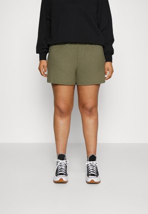 Olive green ribbed shorts with an elastic waistband, paired with a black long-sleeve top and black-and-white sneakers.