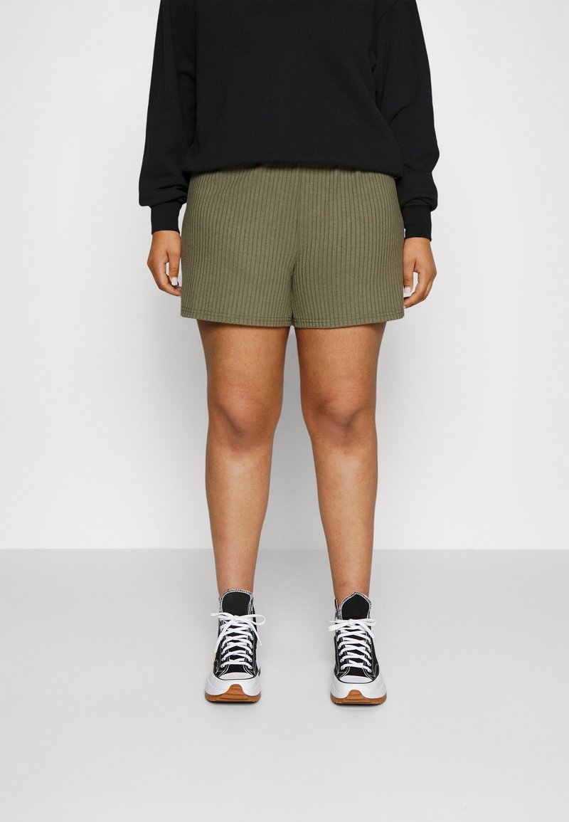 Shorts côtelés vert olive avec une taille élastique, associés à un haut à manches longues noir et des baskets noir et blanc.