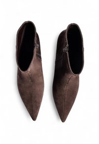 Bottines en suède marron avec des bouts pointus, des fermetures éclairs sur le côté et une texture lisse. L'élévation au niveau du talon ajoute une silhouette élégante.