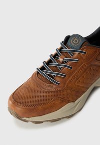 Baskets en cuir marron avec texture perforée, lacets noirs et logo sur la languette. Caractéristiques d'une semelle beige et d'un design à bout rond.